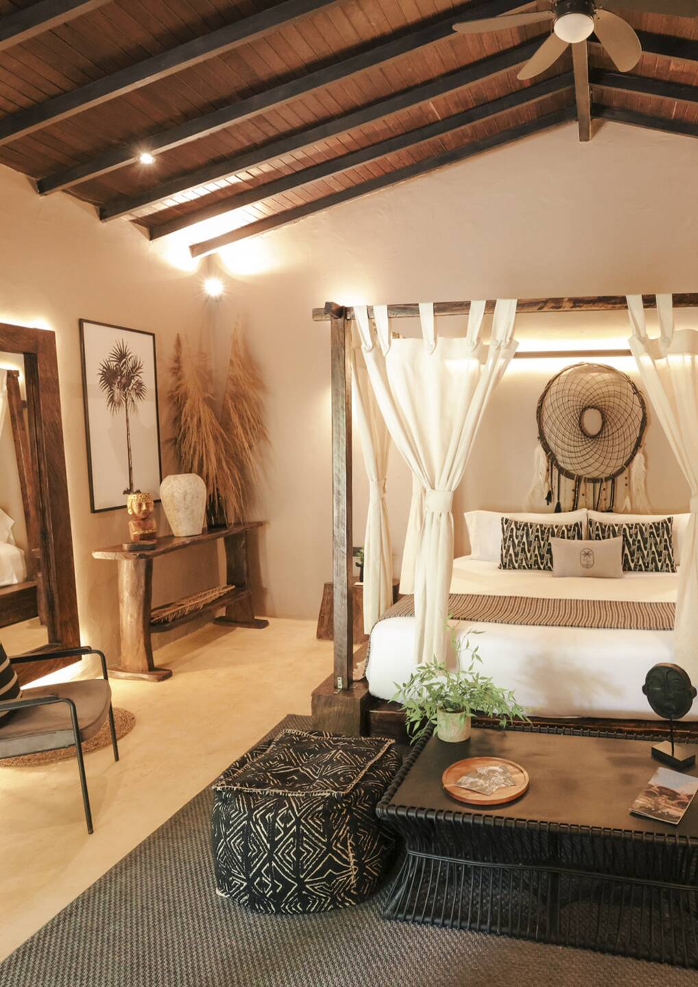 Four-poster bed with white curtains in a warm, tropical-inspired hotel bedroom